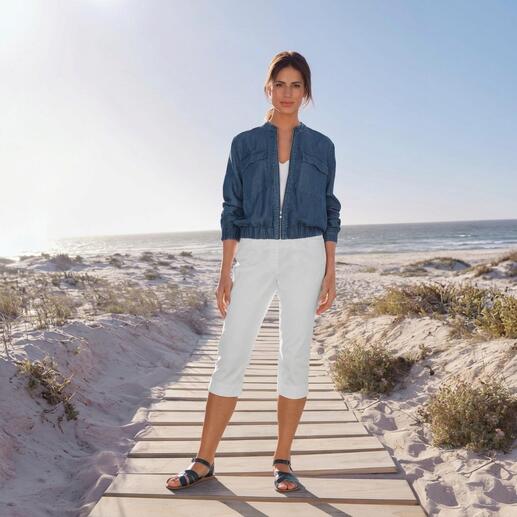 Frau im Light-Denim-Blouson und weißen Caprihosen steht am Strand.