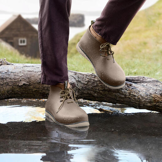 Mann trägt beige Ccilu Regenboots und steht neben einem Baumstamm auf Wasser.