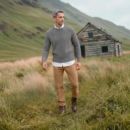 Mann trägt grauen Aran-Pullover in einer grünen Landschaft.