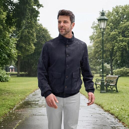 Nähe eines Mannes im Storm-System®-Blouson, der Regen abfängt, blauer Hintergrund.