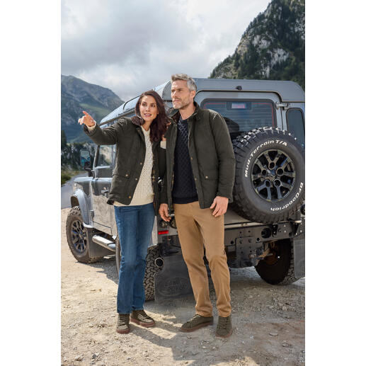 Paar in Outdoorjacken steht vor Geländewagen in sehr natürlicher Umgebung.