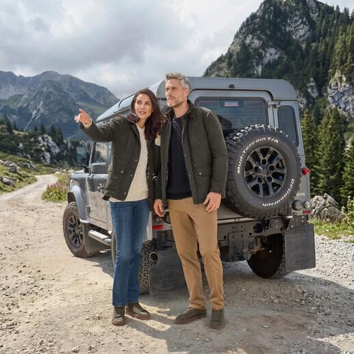 Paar in Outdoorjacken steht vor Geländewagen in sehr natürlicher Umgebung.