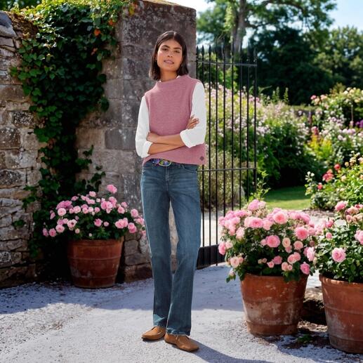 Frau in rosa Walkpullunder über weißem Langarmshirt, steht an einer Blumenpforte.