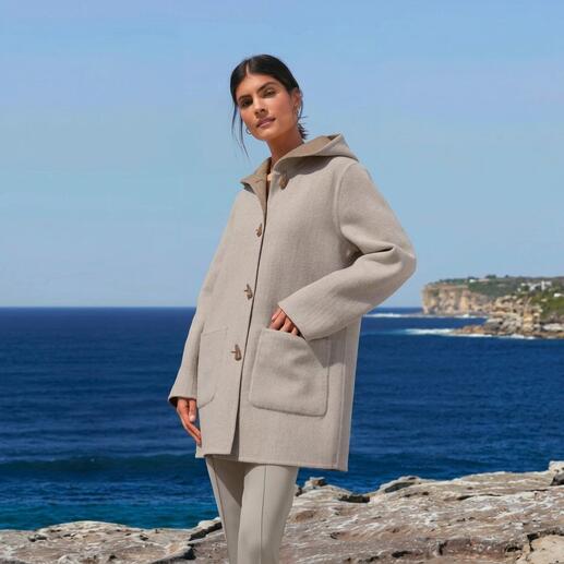 Alpaka-Doubleface-Dufflecoat in Beige, getragen von einer Frau mit Meer im Hintergrund.