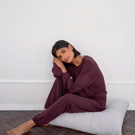 Frau sitzt in einem lila Loungewear Shirt und Hose auf einem Kissen.