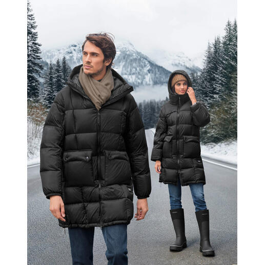 Zwei Personen in schwarzen Daunen-Parkas auf einem winterlichen Straßenabschnitt mit Bergen im Hintergrund.