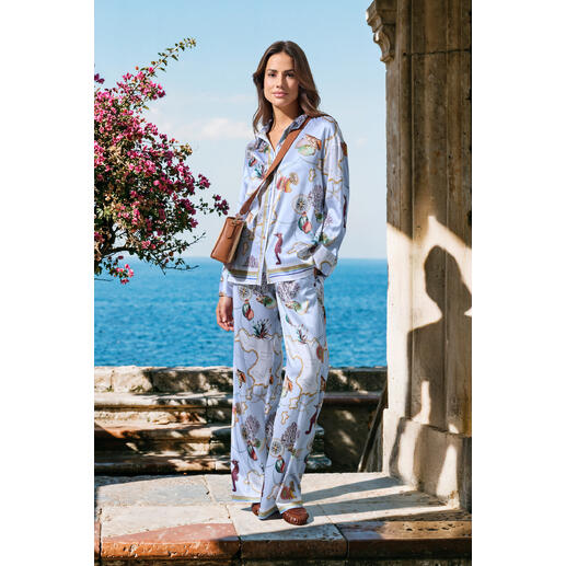 Frau in seidenem pyjama mit buntem Blumenmuster am Meer.