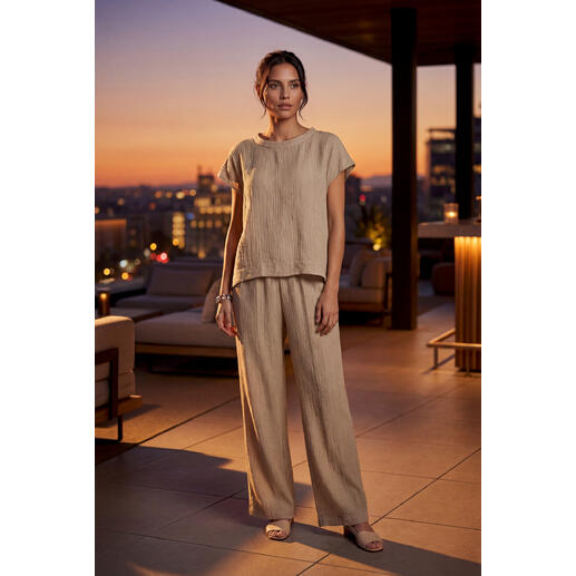 Frau trägt eine sandfarbene Bluse und weite Hose, im Abendlicht.