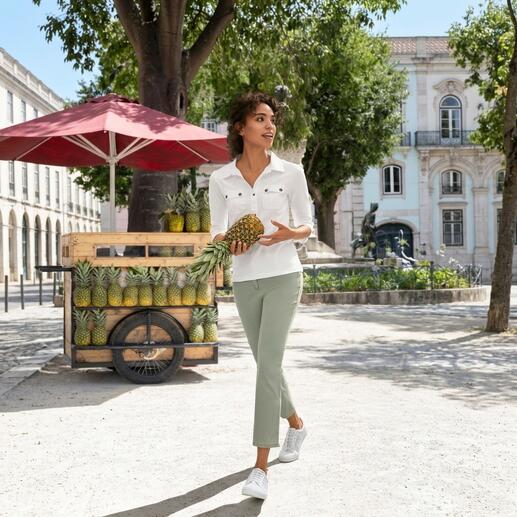 Frau in weißer Bluse und grünen Hosen, hält eine Ananas in der Hand.
