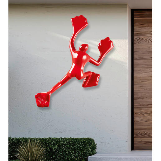 Rotere Skulptur an einer hellen Wand im Außenbereich.