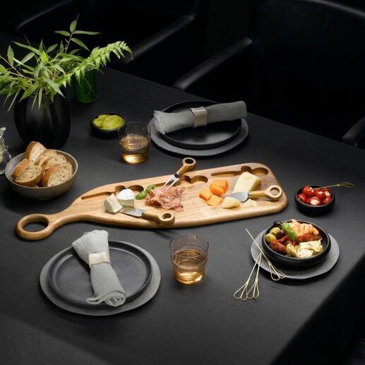 Design-Servierbrett aus Akazienholz mit Käse, Obst und Snacks auf einem dunklen Tisch.