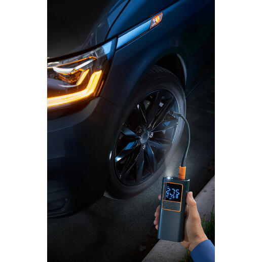 Hand mit Akku-Kompressor-Luftpumpe an einem Autoreifen.