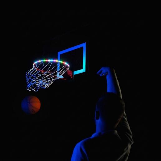 Basketballkorb mit bunten LED-Leuchten und Person beim Werfen auf einem dunklen Platz.