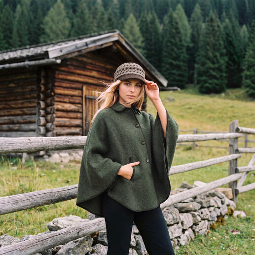 Frau mit grünem Cape und Mütze in einer ländlichen Landschaft