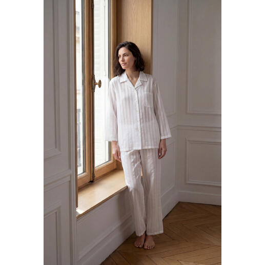 Frau im Baumwoll-Seiden-Streifenpyjama steht am Fenster in einer eleganten Pose