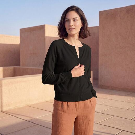 Frau in schwarzem Kurzcardigan steht vor Architektur.