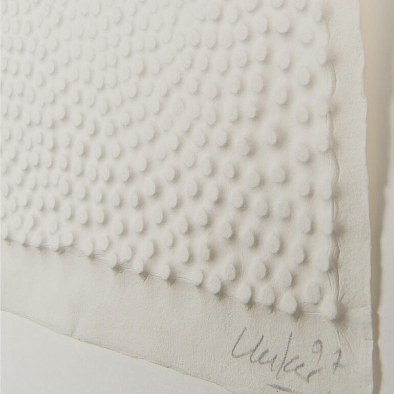 Nägel auf der Druckplatte geben dem angefeuchteten Büttenpapier das prägnante Relief. Detailansicht eines Kunstwerks mit erhabenen Punkten von Günther Uecker.