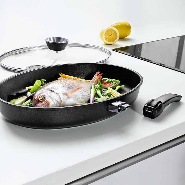 XXL-Aluguss-Fischpfanne mit Fisch und Gemüse auf dem Herd.