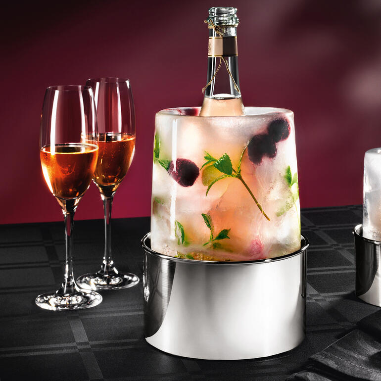 Eis-Cooler mit einer Flasche und Gläsern, umgeben von gefrorenen Früchten.