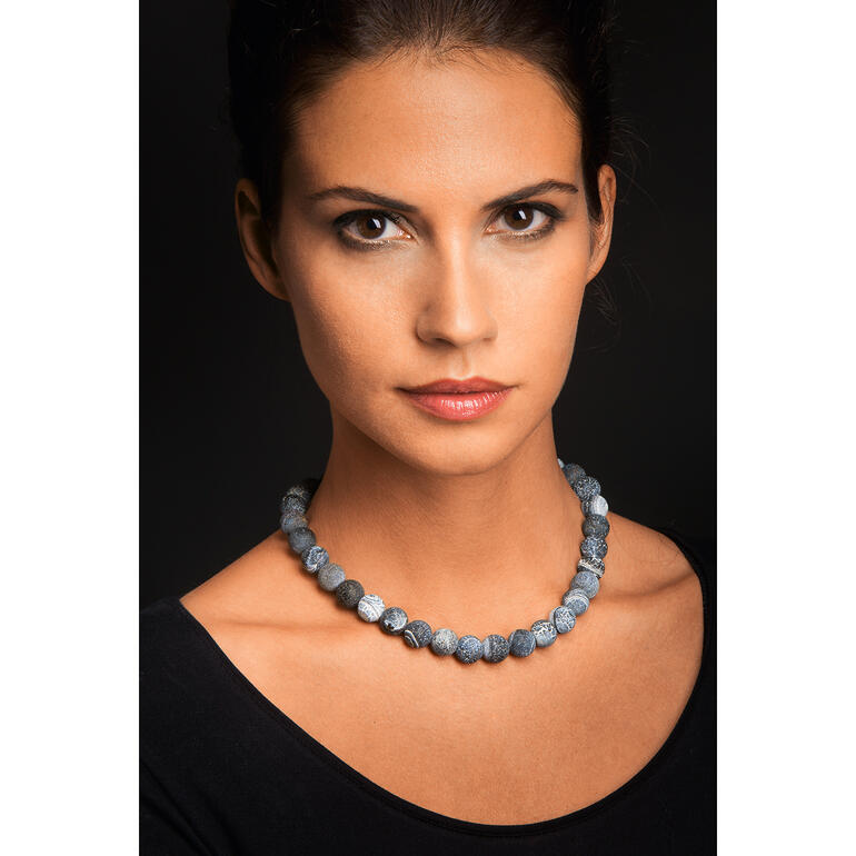 Die graublauen Achate passen perfekt zu legerer und eleganter Kleidung. Frau trägt Achat-Collier aus verschiedenen blauen Steinen