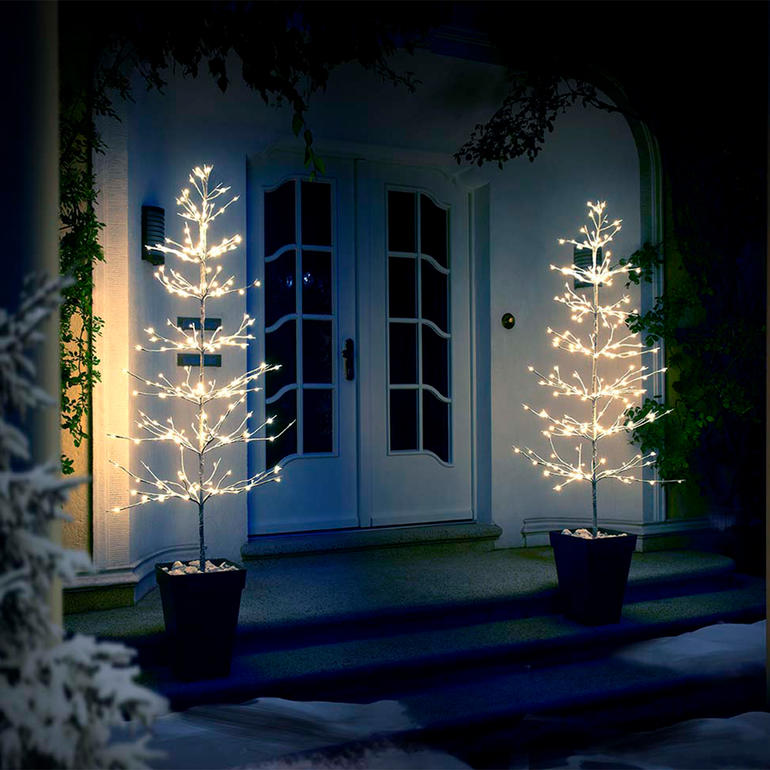 Lichterbaum 90 cm, 120 cm oder 180 cm Zwei beleuchtete Lichterbäume an einer Haustür in der Nacht.