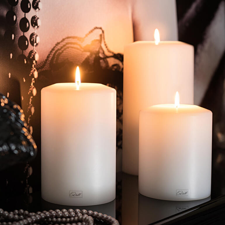 Drei weiße Dauerkerzen mit flammendem Docht auf einem Tisch