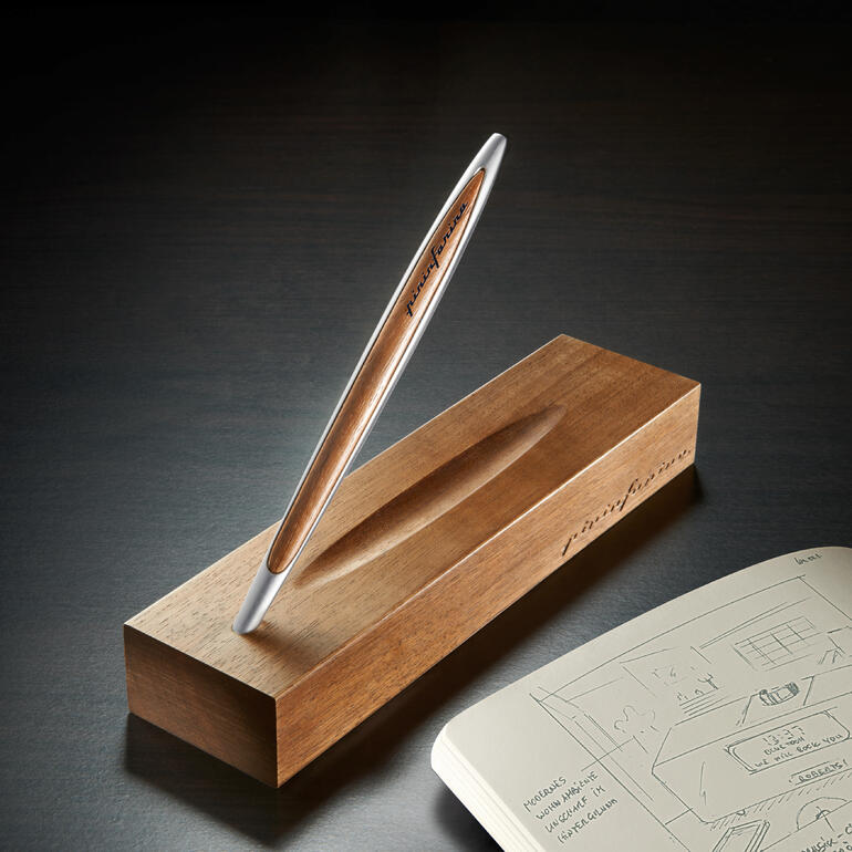 Eleganter Pininfarina Ethergraf®-Stift auf einem Holzblock neben einem Skizzenheft.