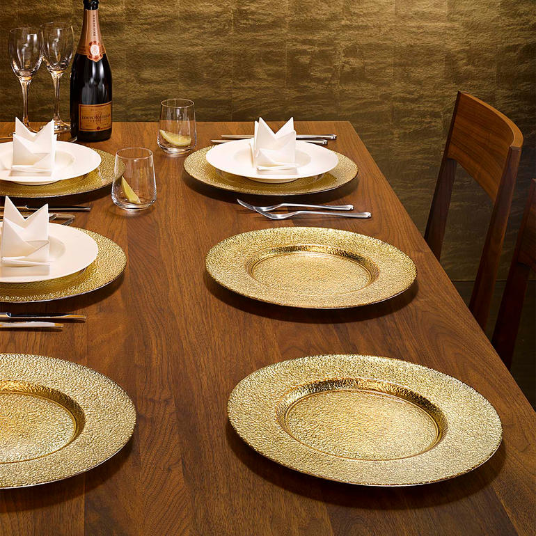 Set aus 6 festlichen Glas-Platztellern mit goldener Oberfläche auf einem gedeckten Tisch.