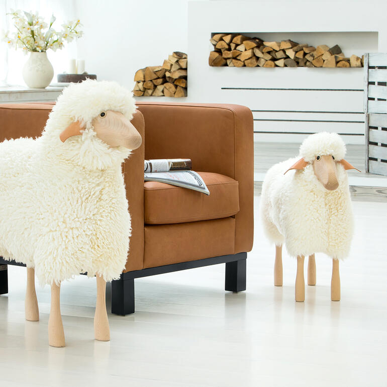 Zwei lebensgroße Schafe aus Plüsch im Wohnraum vor einer Couch.