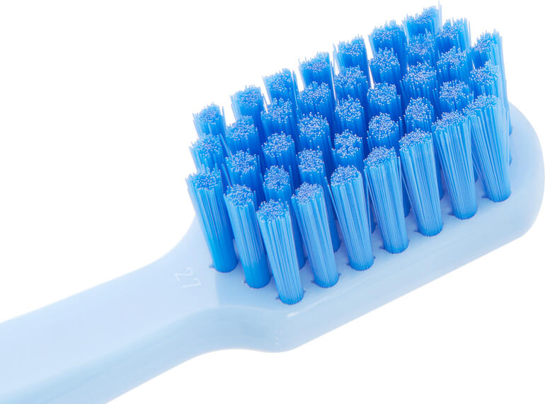 Plaque und Beläge werden durch die extrem feinen Curen®-Filamente besonders gründlich entfernt. Nahaufnahme eines weißen Zahnbürstenkopfes mit blauen Borsten.