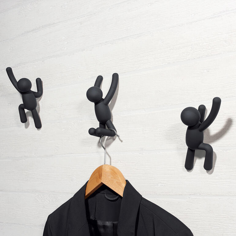 Drei schwarze Garderobenhaken in Form von Kletterern an einer Wand