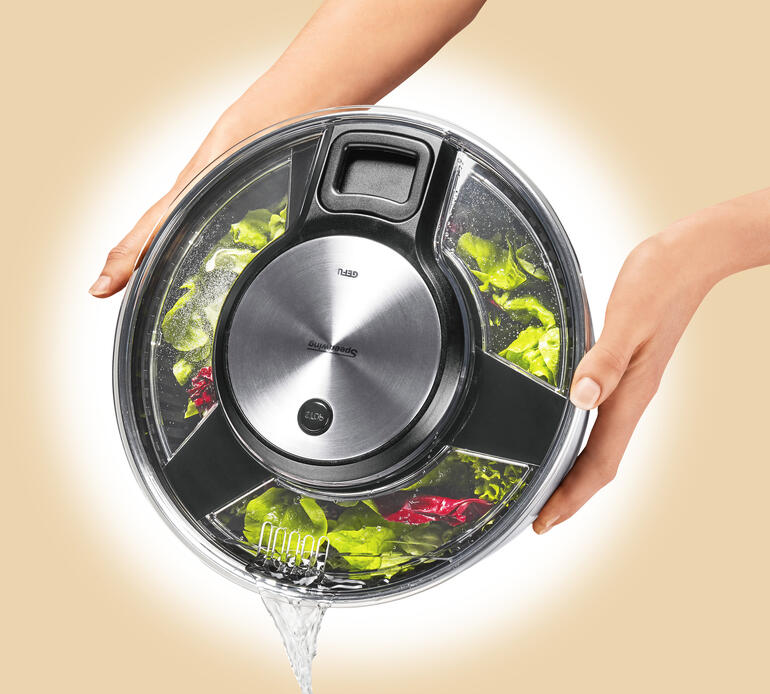 Über Öffnungen im Deckel können Sie das Wasser sauber abgießssen, ohne die Schleuder zu öffnen. Nutzer hält die Salatschleuder mit dem Deckel oben und frischem Gemüse innen.