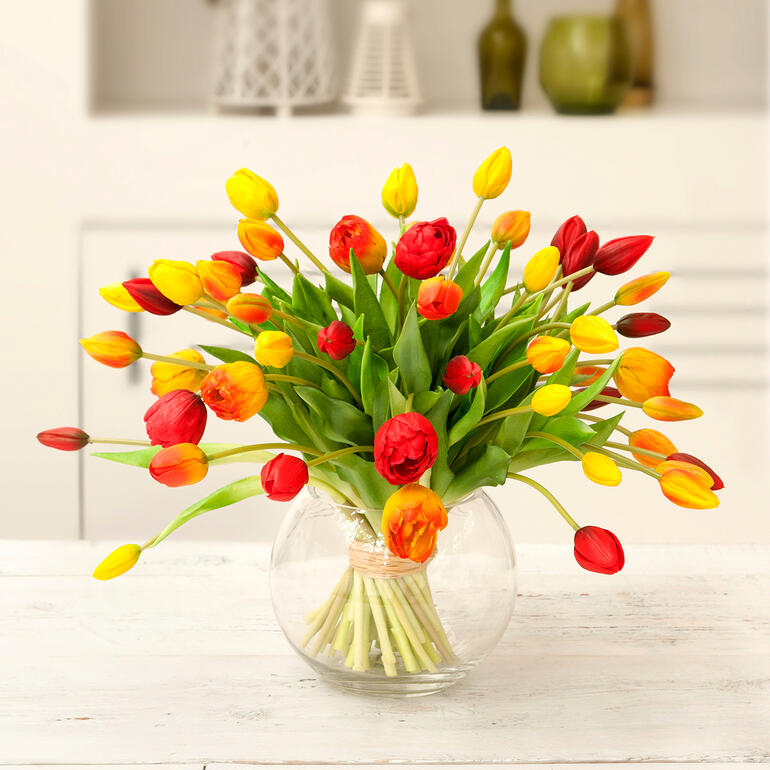 Gelb/Orange/Rot Bunter Tulpenstrauß in einer runden Glas Vase.