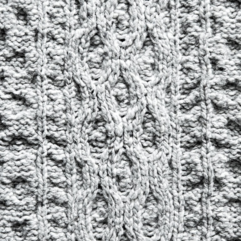 IrelandsEye Aran-Strickplaid Nahaufnahme des Strickmusters eines grauen Plaids.