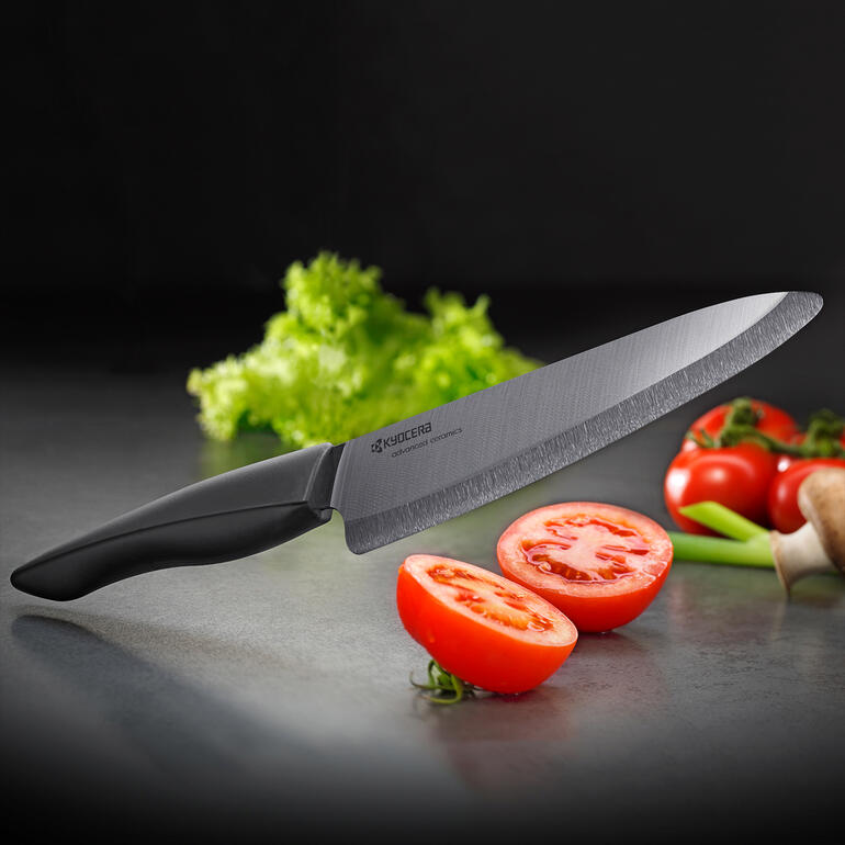 Zirkonia-Keramik-Messer mit schwarzem Griff auf einer Schneideunterlage neben Tomaten und Salat.