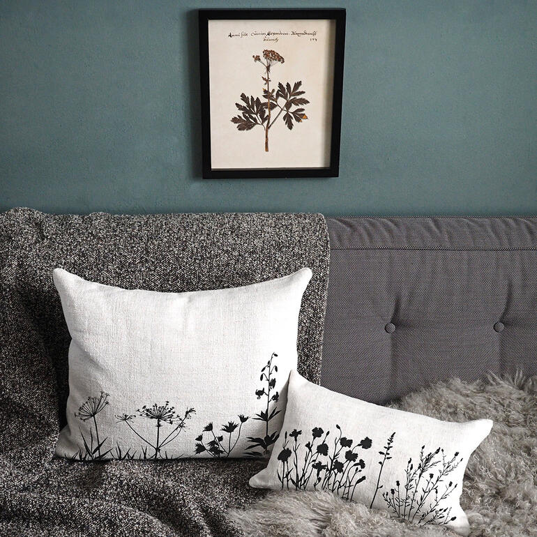 Kissen aus 100 Jahre altem Leinen Zwei Leinenkissen mit schwarzen Pflanzenmustern auf einer Couch, ein Bild hängt darüber.
