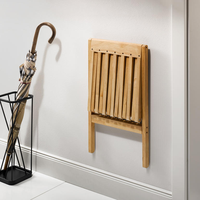 Mit einem Griff platzsparend hochgeklappt. Zusammengeklappter Falt-Wandhocker an der Wand.