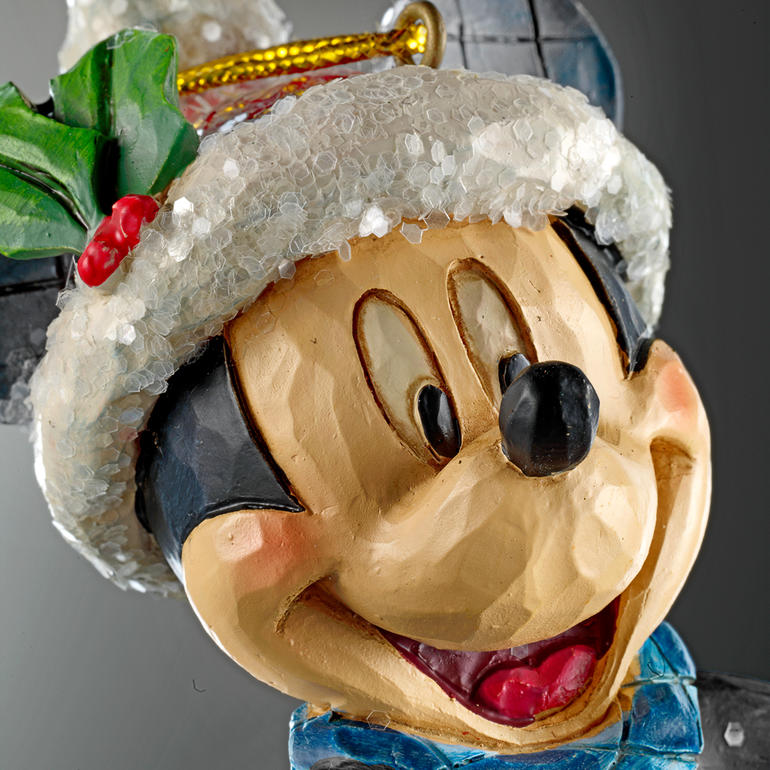 Kunstvoll wie aus einem Stück Holz geschnitzt. Details von Mickey Mouse mit Weihnachtsmütze und grünem Schal, fröhliches Gesicht.