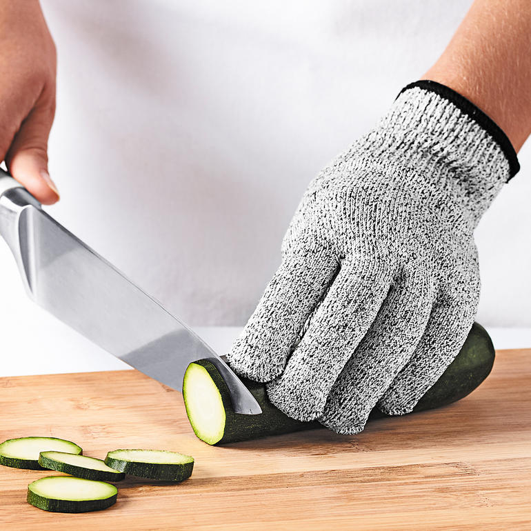 Fingerfertigkeit und Tastgefühl bleiben bewahrt. Hand mit Mastrad Schutzhandschuh schneidet eine Gurke auf Holzbrett.