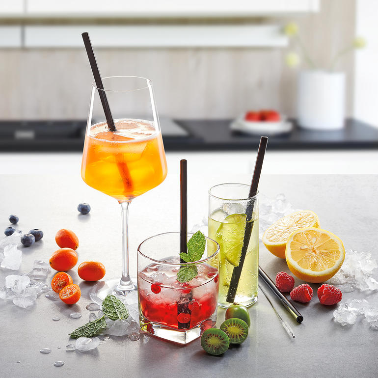 Drei Drinks mit Glastrinkhalmen und Früchten dekoriert auf einer Tischoberfläche.