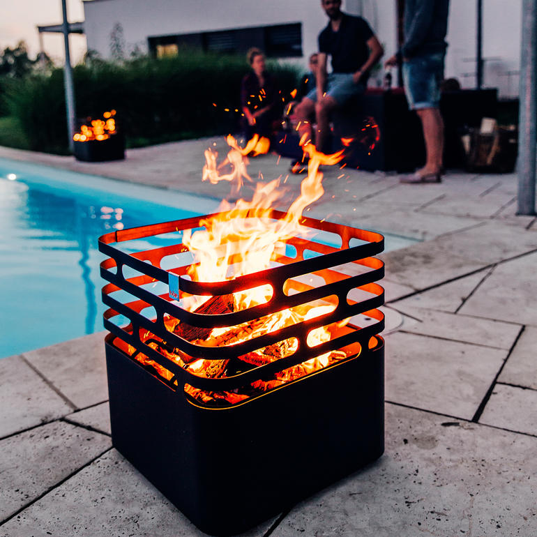 Cube Feuerwehrkorb mit loderndem Feuer, Menschen im Hintergrund.
