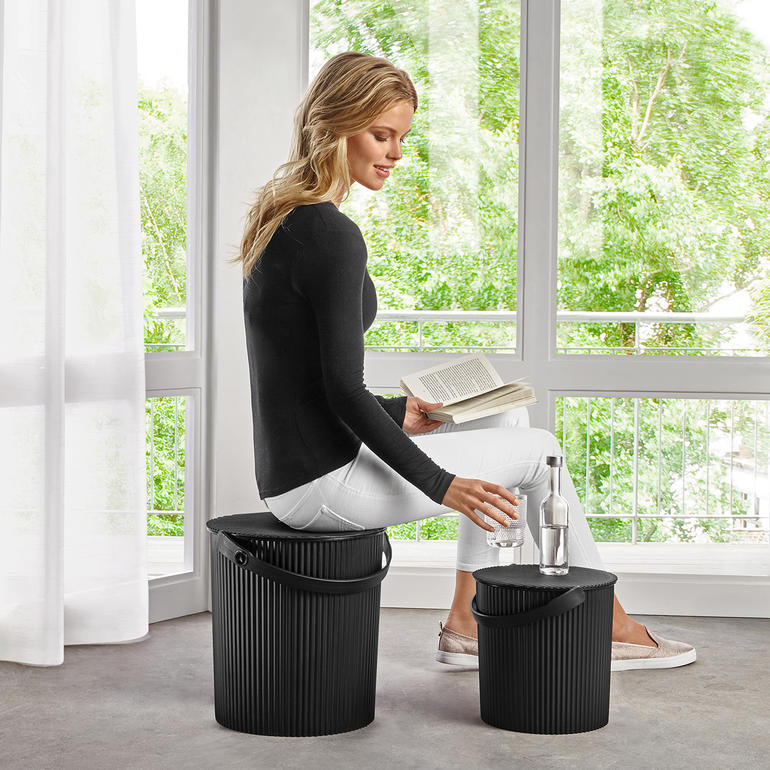 Frau sitzt auf einem Multi Design Bucket und liest ein Buch.