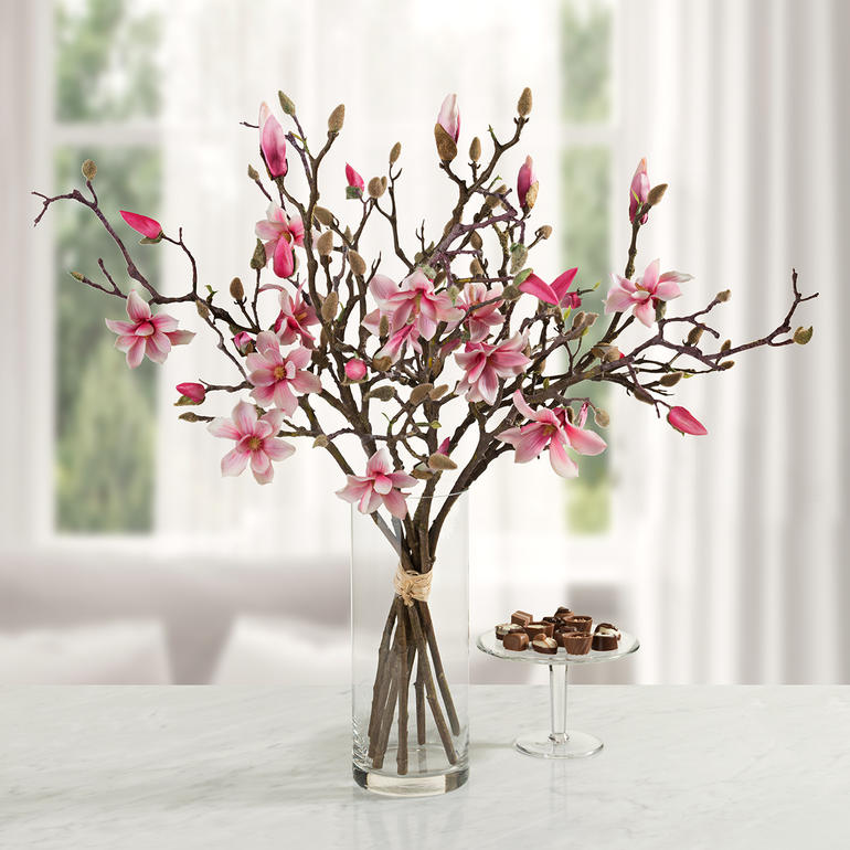 Magnolienstrauß in einer Glasvase, mit rosa Blüten vor einem hellen Hintergrund.