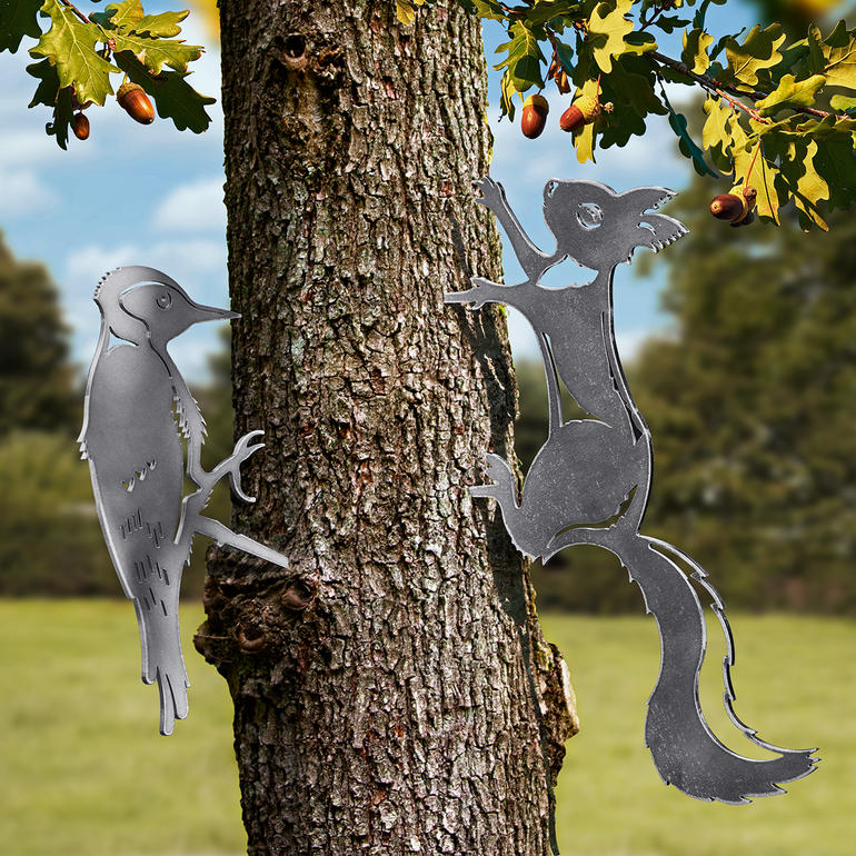 Metallene Kontur-Tiermotive von einem Specht und einem Eichhörnchen an einem Baum.