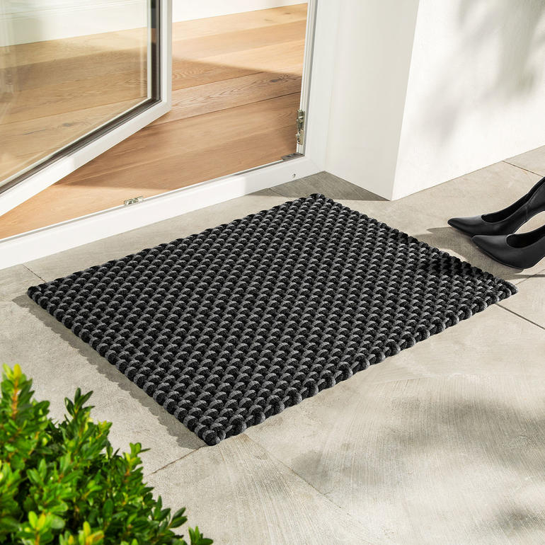 Die Kordelmatte Standard in schwarz/grau (72 x 52 cm) – perfekt auch als Fußmatte. Schwarze/graue Kordelmatte vor einer Tür auf dem Boden.
