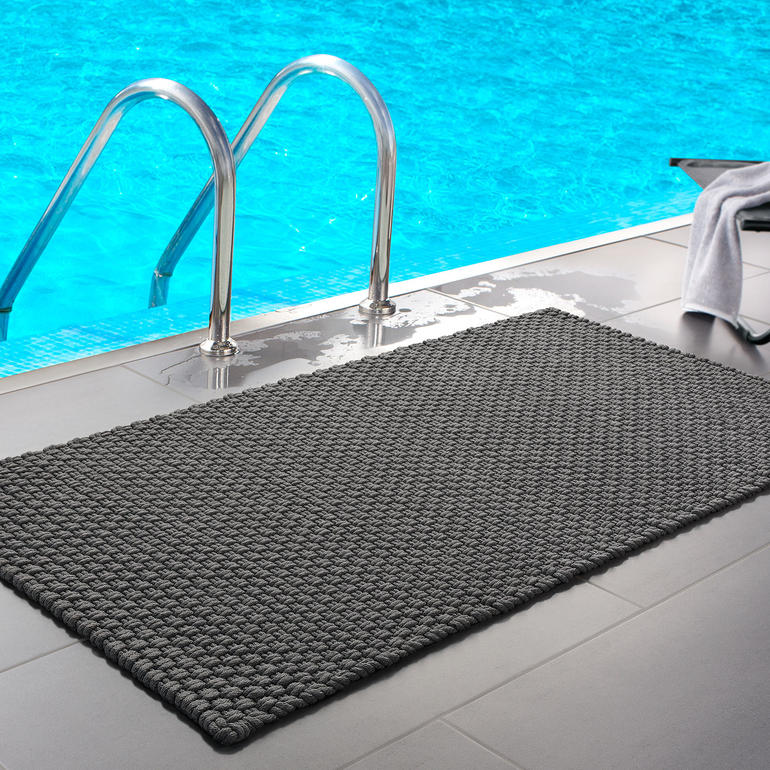 Schwarze Kordelmatte am Poolrand vor blauem Wasser.