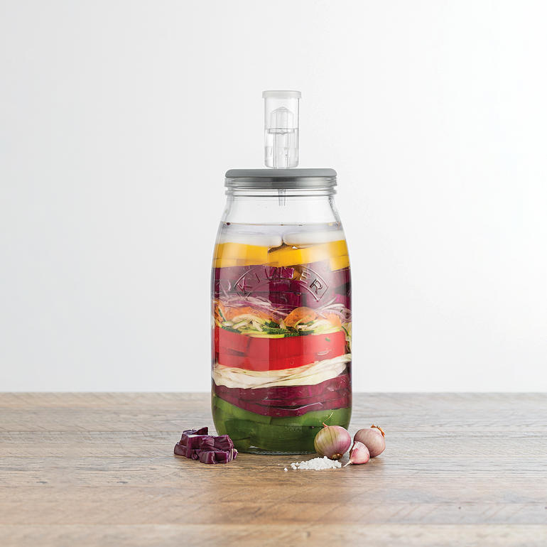 Dank des Gärventils im luftdichten Deckel entsteht kein Überdruck im Glas – für perfektes Gelingen Ihrer Delikatessen. Fermentierglas mit Gärventil, gefüllt mit buntem Gemüse in Schichten.