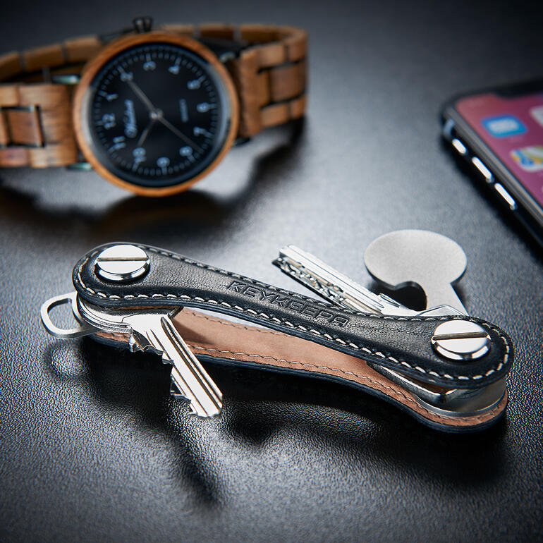 Schlüsselhalter aus Leder mit Schlüsseln, zeitgenössisch auf einem Tisch mit einer Armbanduhr und einem Smartphone.