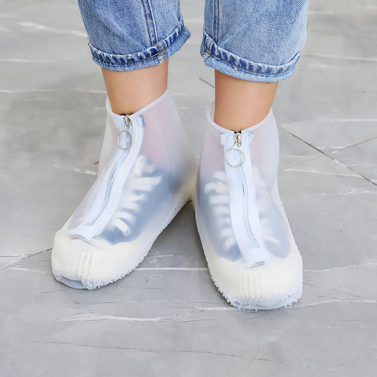 Ausblick auf Damenfüße in weißen Regen-Überschuhen.