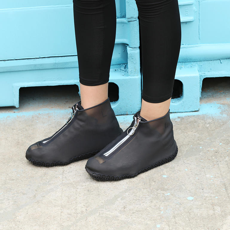 Person steht in schwarzen Regen-Überschuhen vor einer blauen Wand.